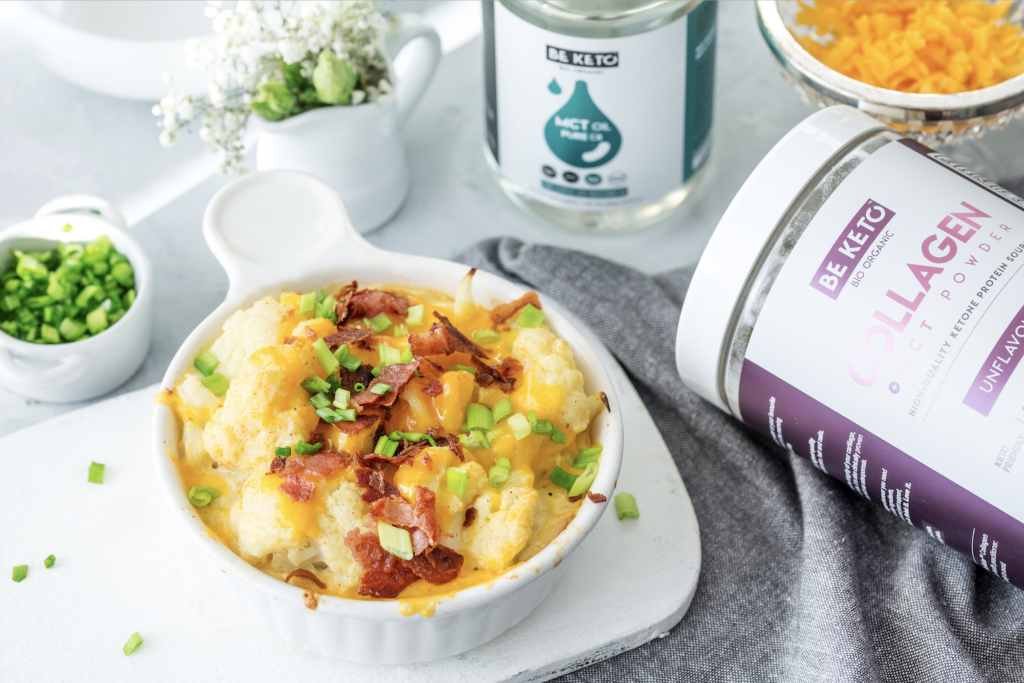 Biała miseczka. W miseczce gratin z kalafonia, posypany serem, szczypiorkiem i boczkiem. W tle mała miseczka z szczypiorkiem, wazonik z kwiatkami, olej MCT C8 i starty ser w misce. Po prawej strony kolagen z MCT w proszku, bezsmakowy