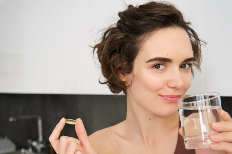 Kobieta w kuchni trzyma kapsułkę omega-3 i szklankę wody